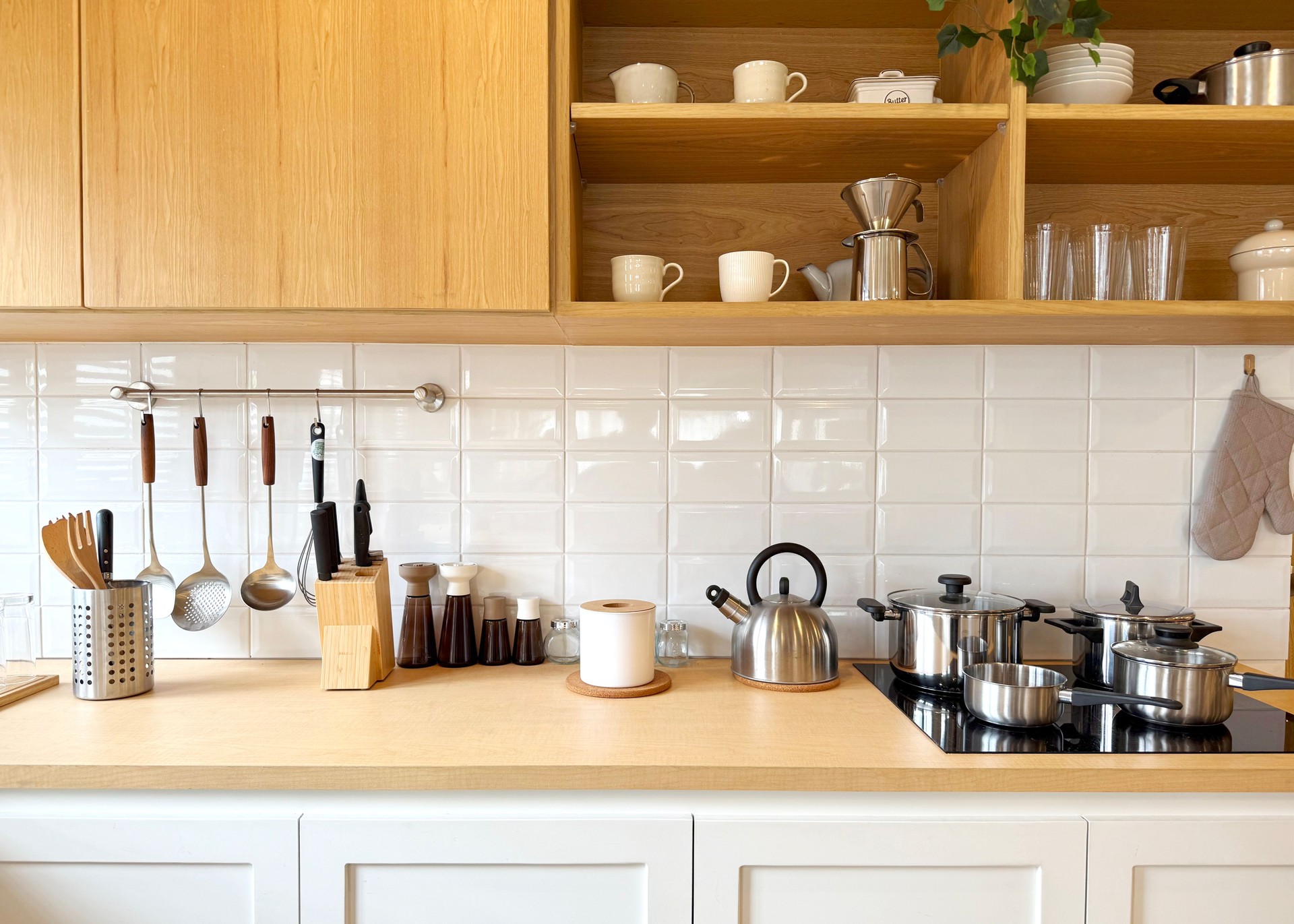 Clean and organized modern kitchen interior with wooden cabinets, white tiled backsplash, and stainless steel appliances. Minimalist Scandinavian style, cozy home cooking space.